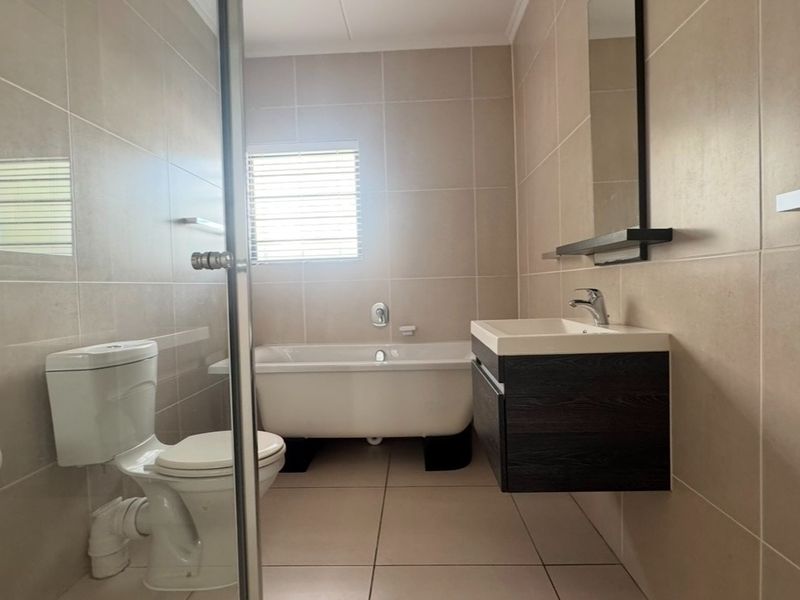 Modern bathroom featuring a freestanding bathtub, wall-mounted vanity, glass shower enclosure, and neutral floor-to-ceiling tiling.