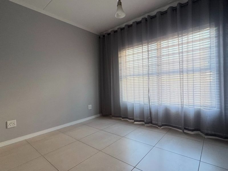 A clean, empty bedroom featuring neutral tiled flooring, grey walls, and a built-in cupboard, offering a versatile space ready for personalization.