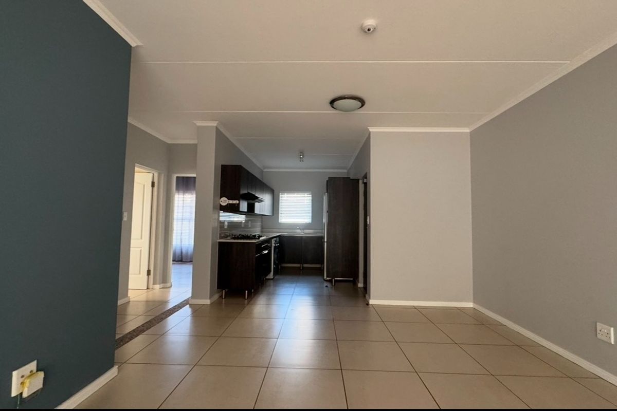 An open-plan living and kitchen area featuring neutral tiled flooring, modern dark cabinetry, and integrated kitchen appliances in a clean, well-maintained space.