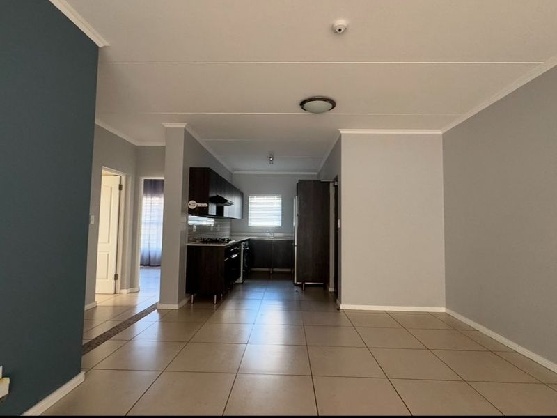 An open-plan living and kitchen area featuring neutral tiled flooring, modern dark cabinetry, and integrated kitchen appliances in a clean, well-maintained space.