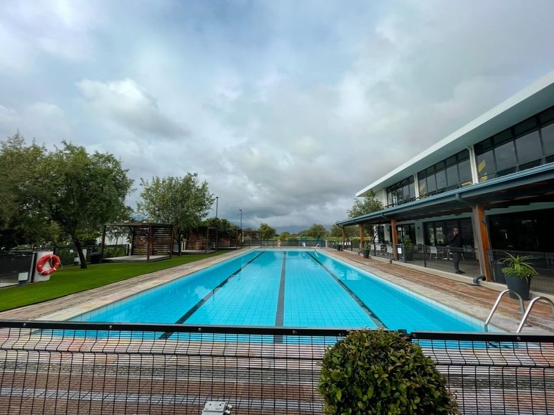 A well-maintained lap swimming pool area featuring a surrounding deck, metal safety fencing, and adjacent covered patio space within a landscaped complex.