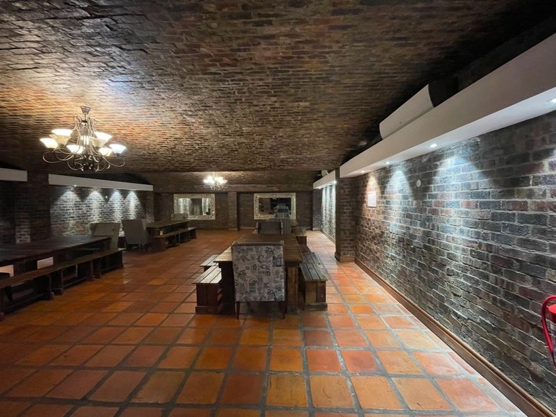 Spacious clubhouse area featuring a distinctive exposed brick vaulted ceiling, terracotta tile flooring, and ambient recessed lighting, creating a warm and rustic atmosphere.