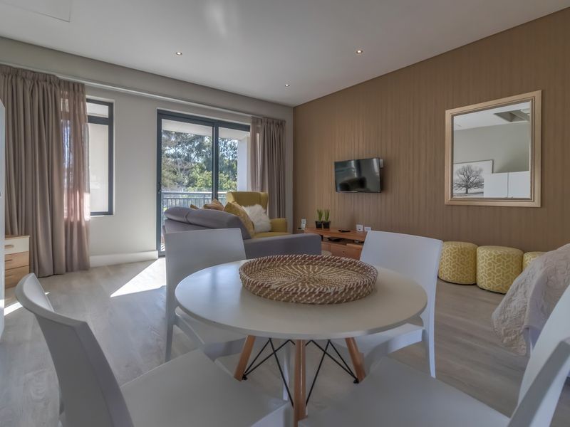 Modern open-plan living area featuring wood-look laminate flooring, recessed downlighting, and a sliding glass door leading to a private balcony.
