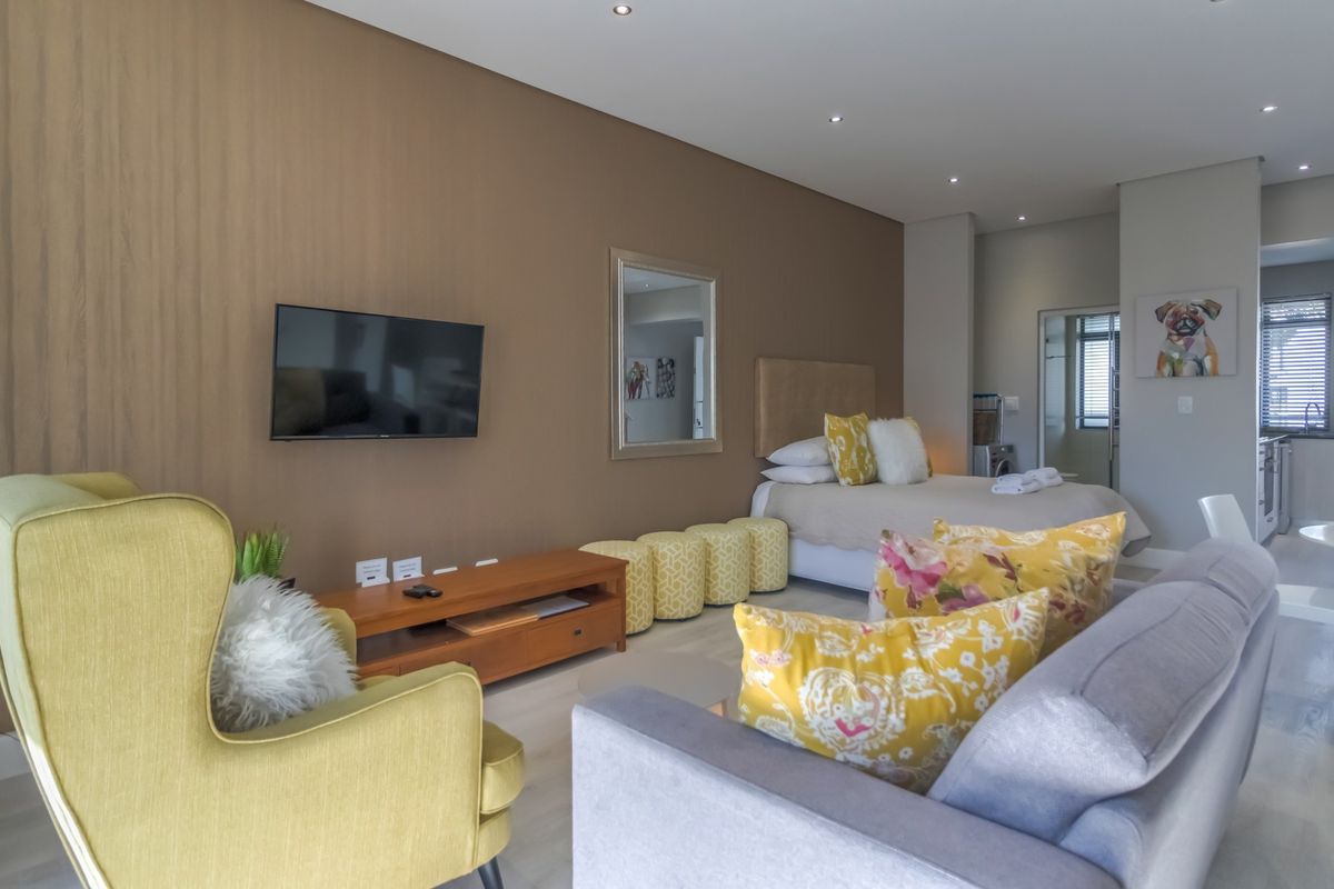 Modern open-plan apartment featuring a combined living and bedroom area with neutral tones, recessed lighting, and sleek laminate flooring throughout.