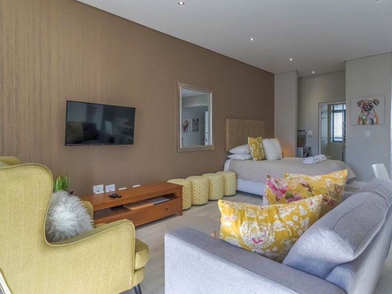 Modern open-plan apartment featuring a combined living and bedroom area with neutral tones, recessed lighting, and sleek laminate flooring throughout.
