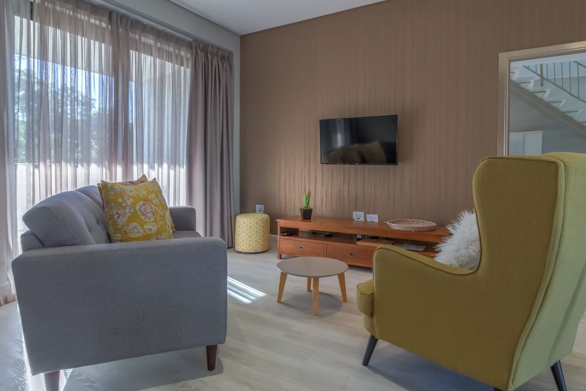 A well-lit living room featuring light laminate flooring, textured feature wall, and floor-to-ceiling sheer curtains providing natural light.