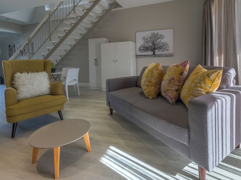 A bright and modern living room featuring light laminate flooring and an open-plan staircase leading to the upper level.