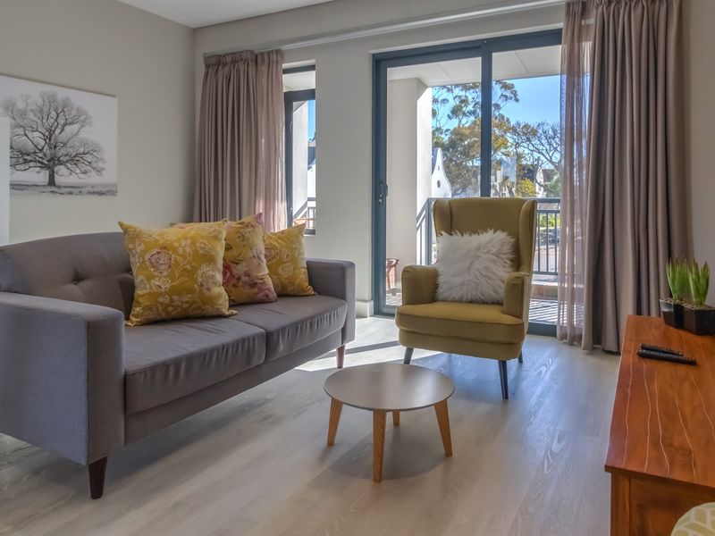 A bright and well-maintained living room featuring modern laminate flooring and a large sliding glass door providing access to an outdoor balcony.