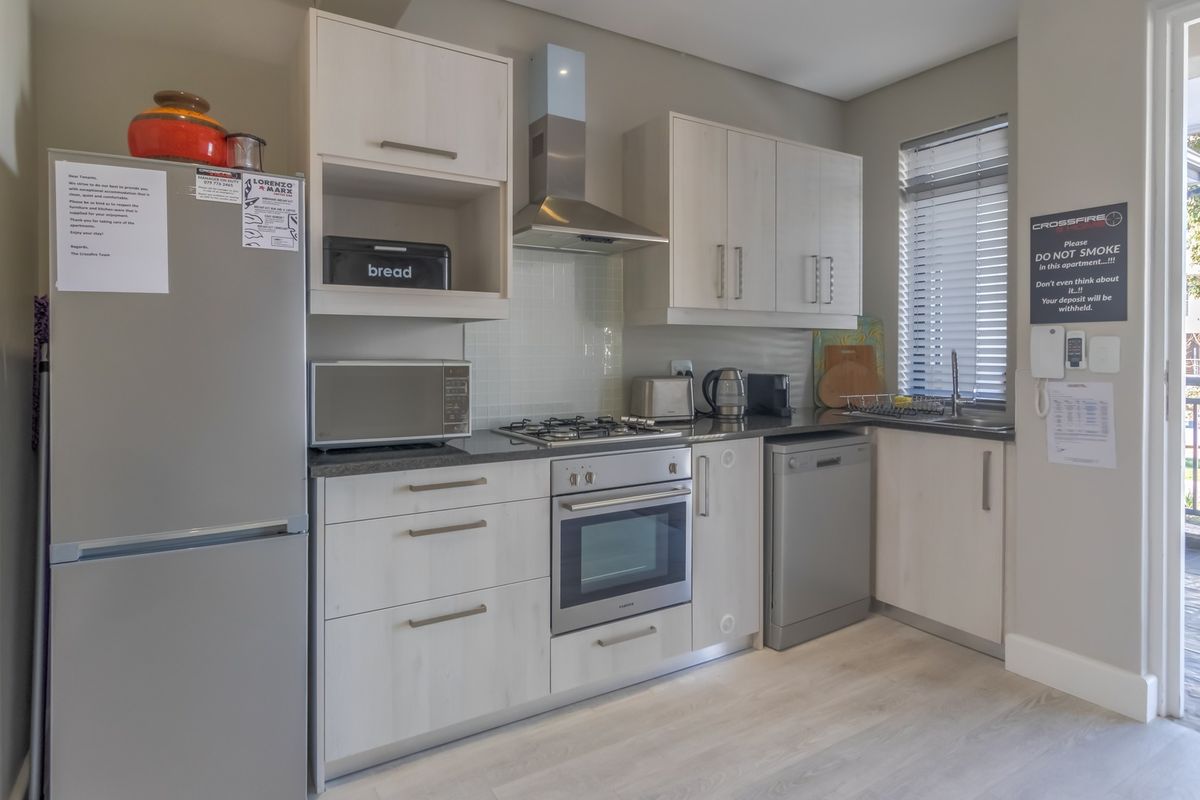 Modern kitchen featuring light wood cabinetry, stainless steel appliances including a gas hob and oven, tiled backsplash, and laminate flooring.