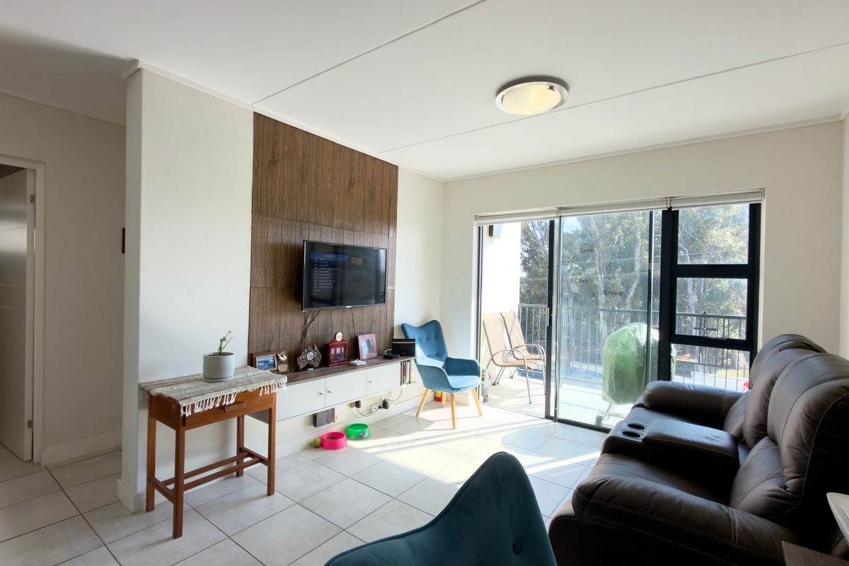 A bright living room featuring tiled floors, a wood-paneled feature wall with a built-in media console, and sliding glass doors leading to a balcony.