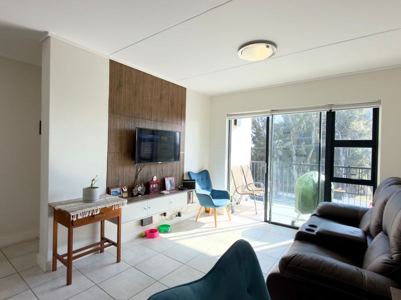 A bright living room featuring tiled floors, a wood-paneled feature wall with a built-in media console, and sliding glass doors leading to a balcony.