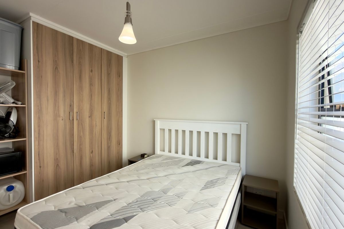 A well-maintained bedroom featuring wood-finish built-in wardrobes, neutral walls, and venetian blinds allowing natural light.