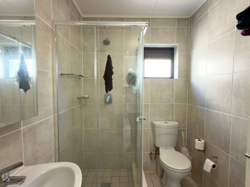 A modern bathroom featuring neutral wall and floor tiling, a glass shower enclosure, a white toilet, and a wall-mounted washbasin with a mirror.