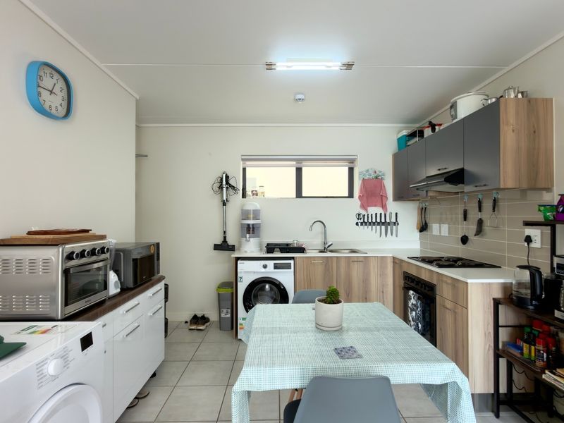 Functional kitchen featuring modern wood-look cabinetry, tiled backsplash, gas hob, extractor fan, and integrated laundry plumbing, offering a practical and well-organized workspace.