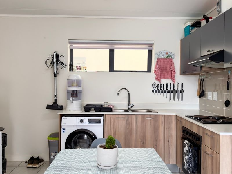 A functional kitchen featuring wood-look cabinetry, integrated washing machine, built-in oven with hob, and a tiled backsplash with ample counter space.