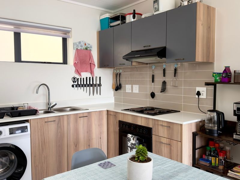 Modern kitchen featuring wood-grain cabinetry, light countertops, tiled backsplash, integrated washing machine, and built-in cooking appliances.