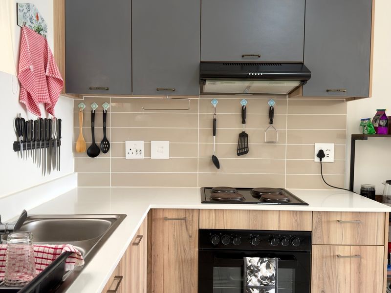 Modern kitchen featuring grey upper cabinets, wood-grain lower cabinetry, a built-in oven with electric hob, and a clean tiled splashback.