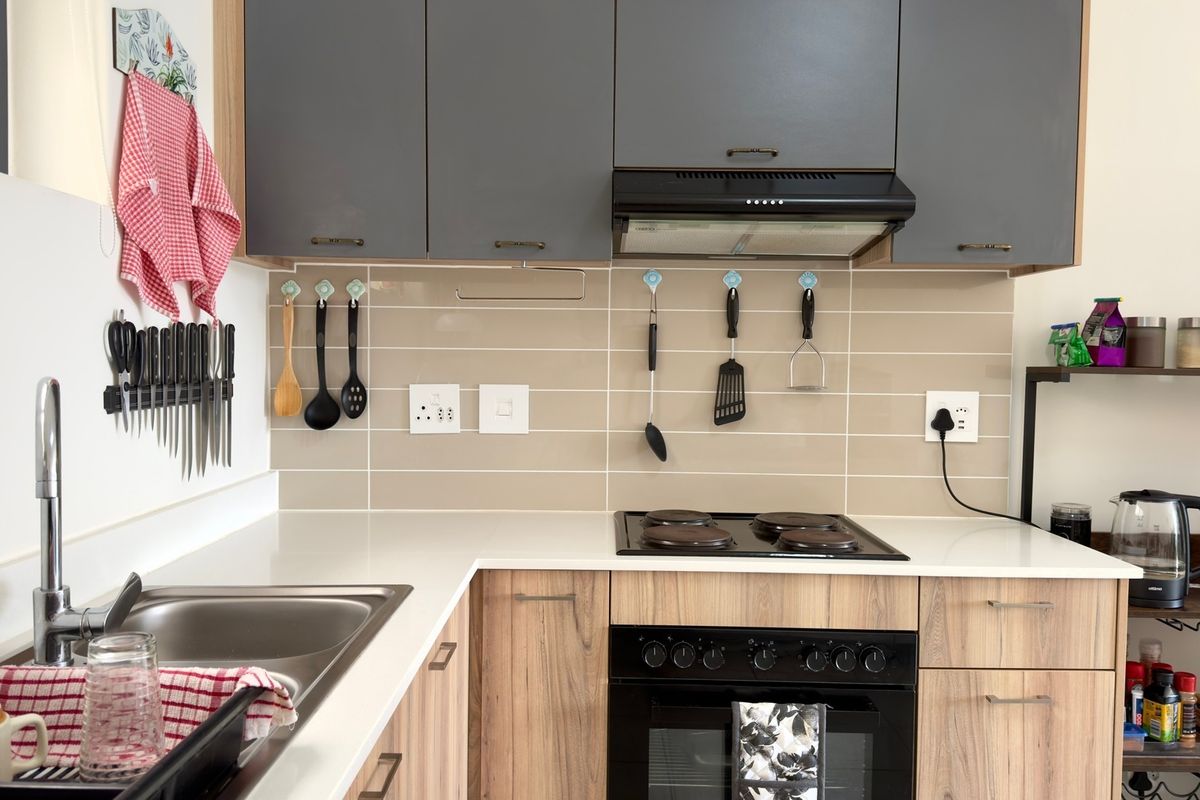 Modern kitchen featuring grey upper cabinets, wood-grain lower cabinetry, a built-in oven with electric hob, and a clean tiled splashback.