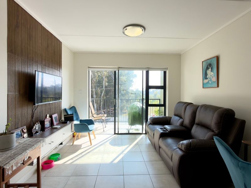A bright living room featuring tiled flooring, a wood-look feature wall, and a sliding glass door providing access to an outdoor balcony area.
