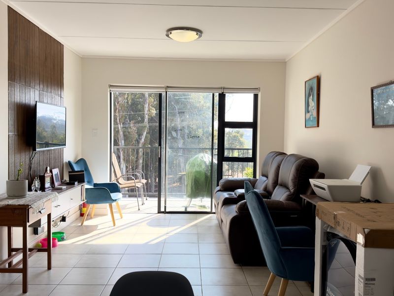 A living room featuring tiled flooring, a wood-look accent wall, and large sliding glass doors providing access to an outdoor balcony area.