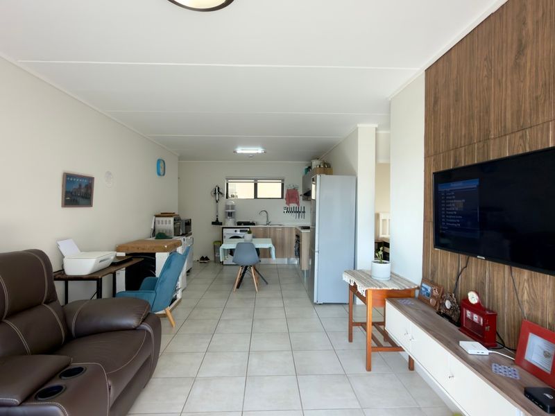 Open-plan living area featuring tiled flooring, a wood-look feature wall, and an integrated kitchen and laundry space.