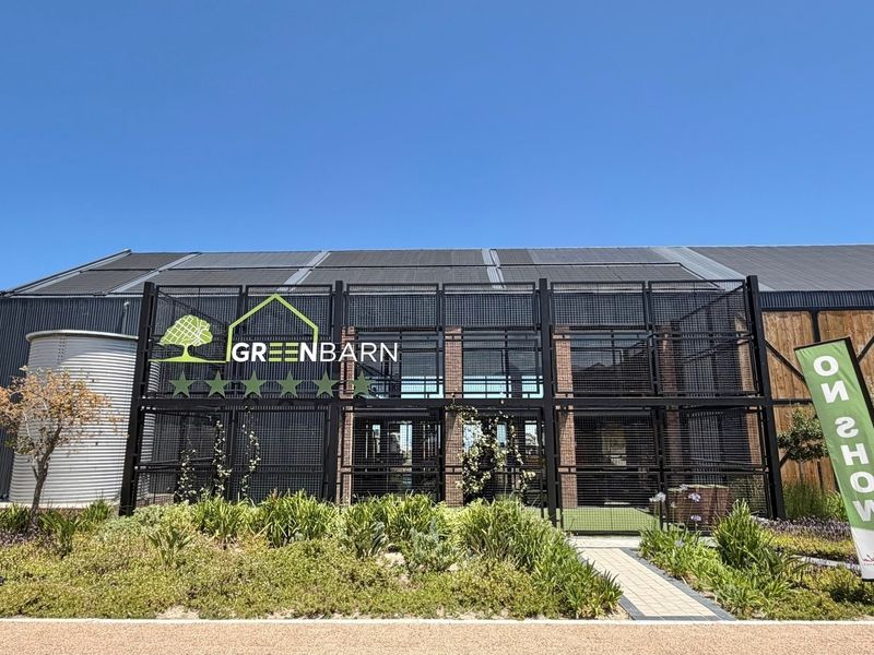 Modern industrial-style building facade featuring metal cladding, integrated solar panels, and a decorative metal mesh entrance structure with landscaped front garden.