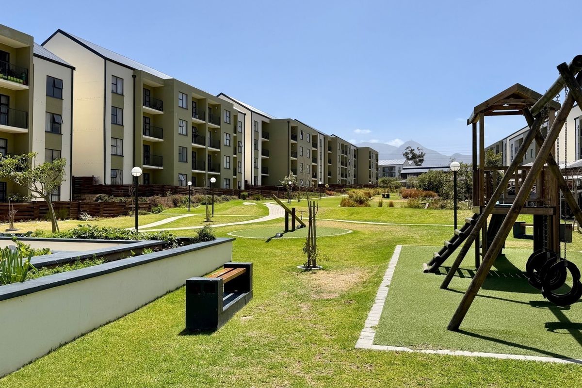 A well-maintained communal garden area within an apartment complex, featuring landscaped lawns, paved walkways, and a children's playground.