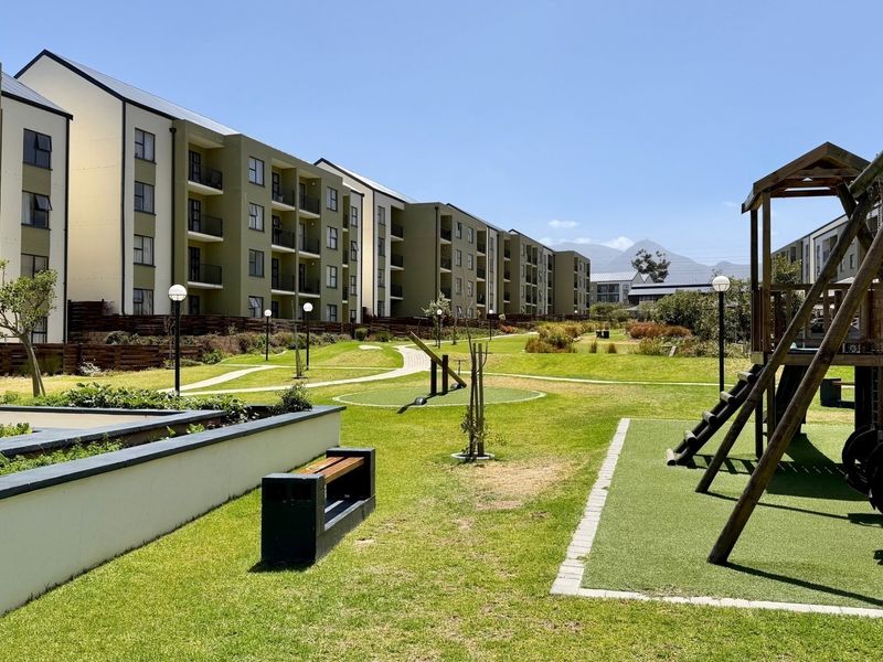 A well-maintained communal garden area within an apartment complex, featuring landscaped lawns, paved walkways, and a children's playground.