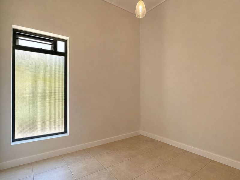 A clean, empty bedroom featuring neutral tiled flooring, a textured glass window for privacy, and a simple pendant light fixture.