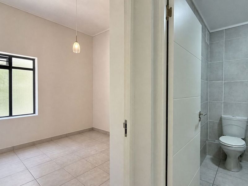An empty bedroom featuring tiled flooring and a pendant light, with an adjacent bathroom visible through the doorway.