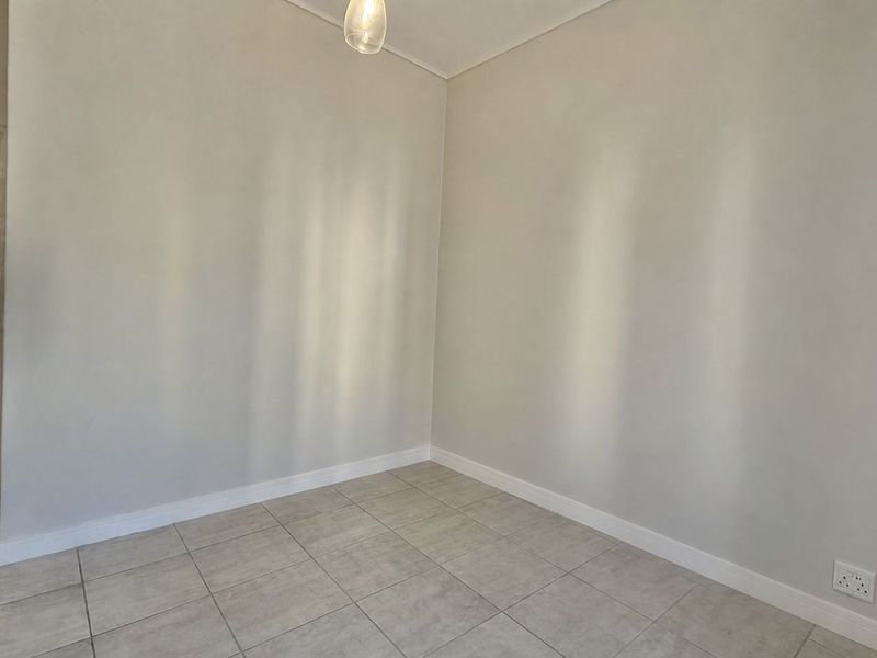 A clean, empty bedroom featuring neutral tiled flooring, white walls, and a simple pendant light fixture, offering a blank canvas for personalization.