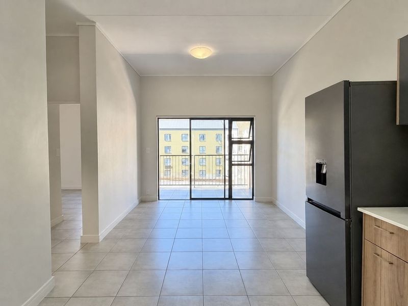 An open-plan living and kitchen area featuring neutral tiled flooring, modern cabinetry, and a sliding glass door leading to a private balcony.