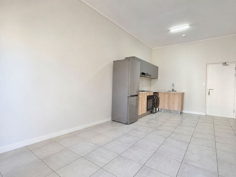 An open-plan living and kitchen area featuring modern built-in cabinetry, tiled flooring, and integrated kitchen appliances in a clean, neutral space.