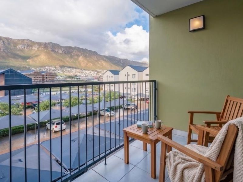A well-maintained balcony featuring tiled flooring, a metal balustrade, and scenic mountain views overlooking the complex parking area.