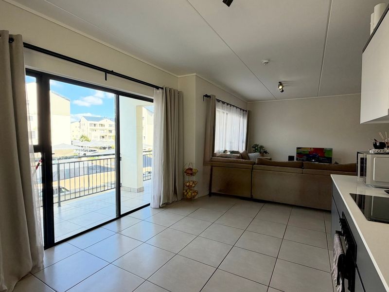 Modern open-plan living area featuring tiled floors, a sleek kitchen with built-in hob, and direct access to a private balcony.