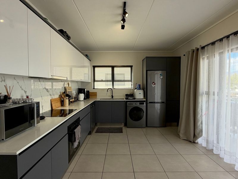 Modern kitchen featuring sleek handleless cabinetry, marble-look splashback, quartz countertops, integrated appliances, and tiled flooring with direct access to the balcony.