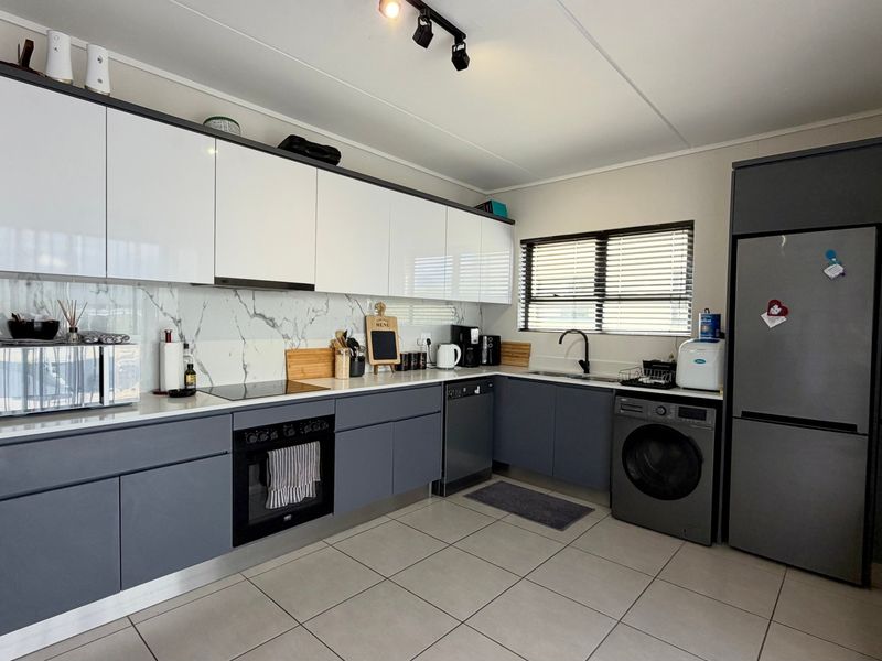 Modern kitchen featuring sleek two-tone cabinetry, marble-effect splashback, integrated oven, electric hob, and tiled flooring with contemporary track lighting.
