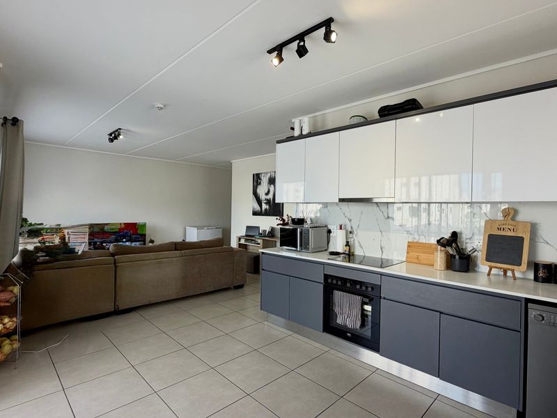 Modern open-plan living area featuring a sleek kitchen with high-gloss cabinetry, marble-look splashback, integrated appliances, and neutral tiled flooring throughout.