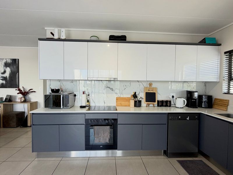 Modern kitchen featuring sleek two-tone cabinetry, marble-look splashback, integrated appliances, and tiled flooring in an open-plan layout.