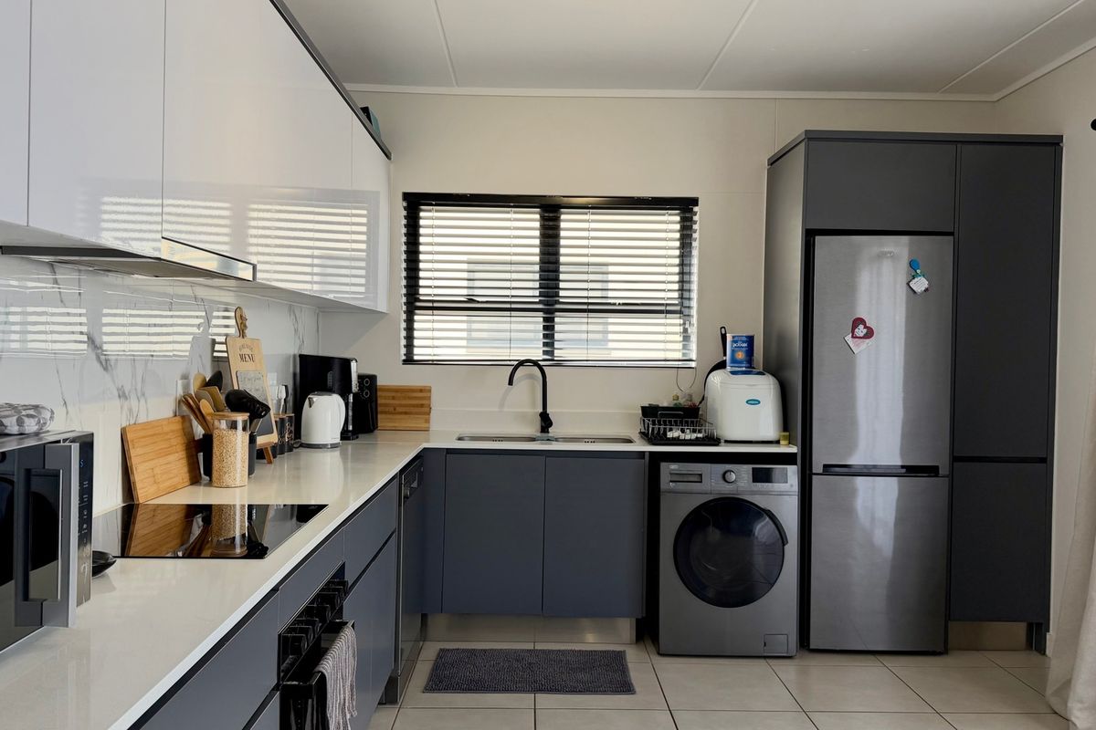 Modern kitchen featuring sleek grey and white cabinetry, quartz countertops, marble-look splashback, integrated appliances, and high-quality finishes throughout.