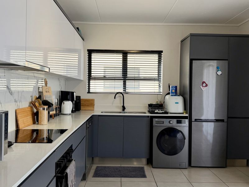 Modern kitchen featuring sleek grey and white cabinetry, quartz countertops, marble-look splashback, integrated appliances, and high-quality finishes throughout.