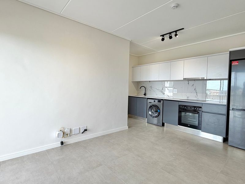 Modern open-plan kitchen featuring sleek two-tone cabinetry, marble-look splashback, integrated oven, and tiled flooring in a clean, contemporary apartment setting.