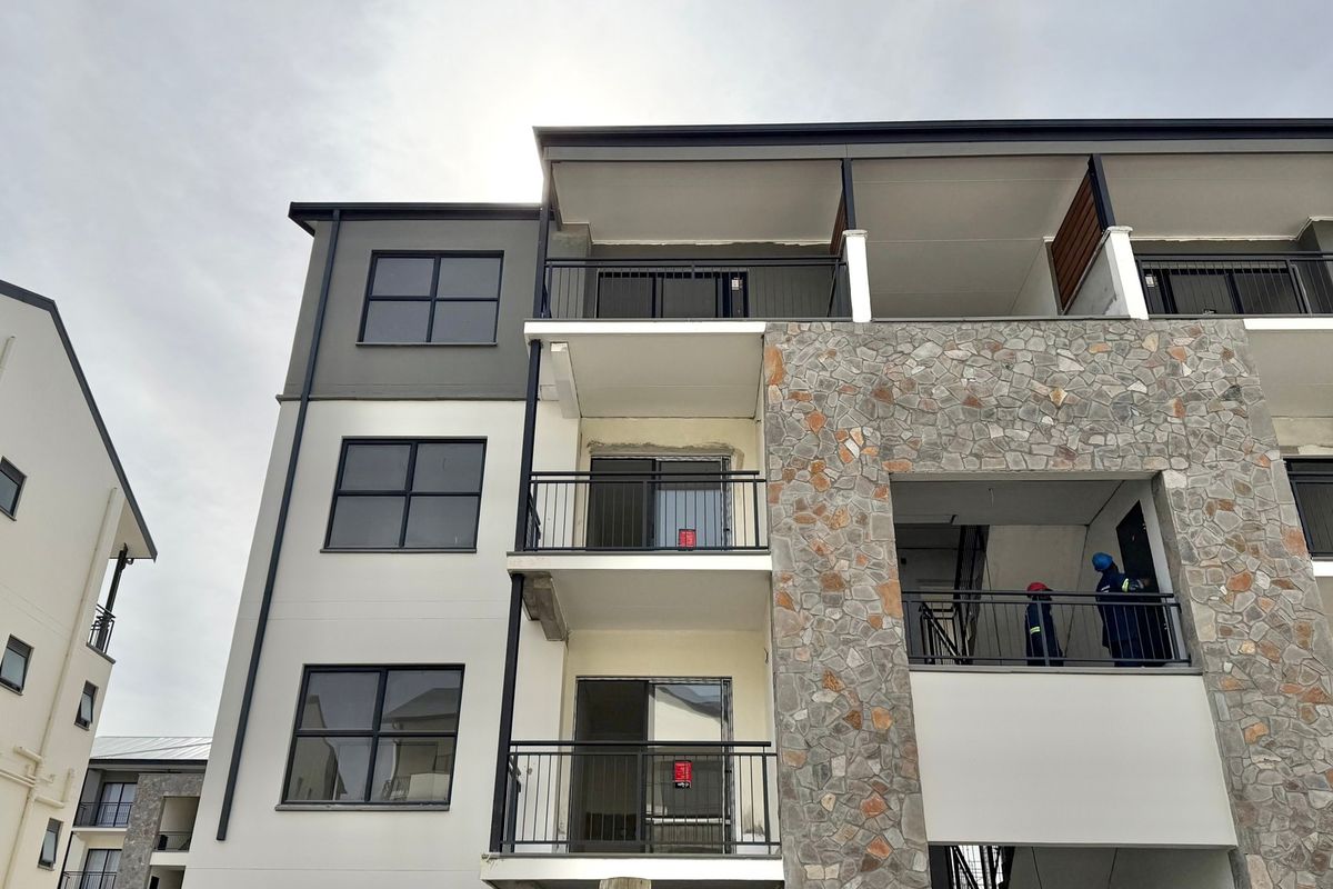 Exterior view of a modern apartment building featuring stone cladding, metal balcony railings, and large aluminum-framed windows under construction.