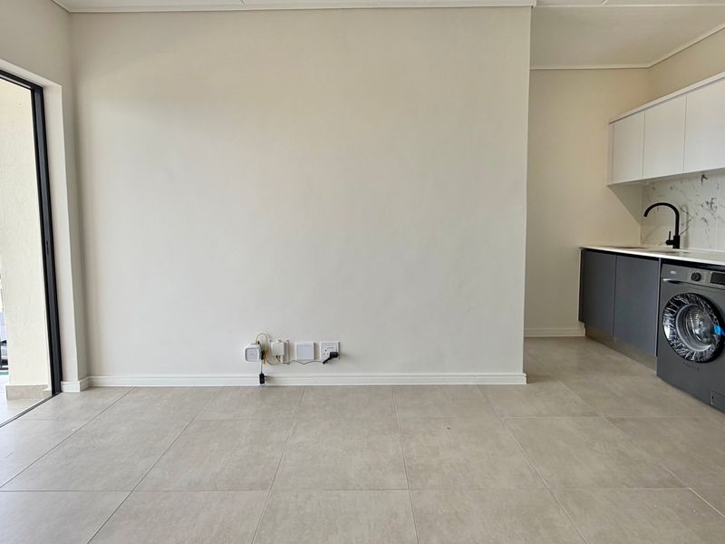 Modern open-plan living area featuring neutral tiled floors, a sleek kitchen with integrated appliances, and direct access to a private balcony.
