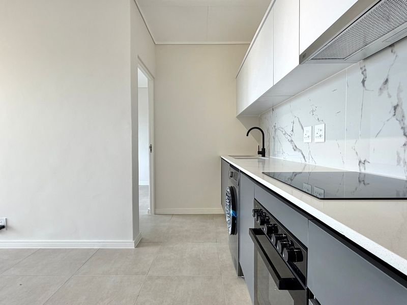 Modern kitchen featuring sleek grey cabinetry, quartz countertops, marble-look splashback, built-in oven, and hob, with clean tiled flooring throughout.