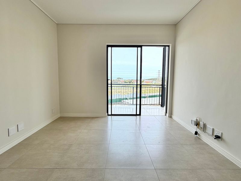 A bright, empty living area featuring neutral tiled flooring and a sliding glass door providing access to a balcony with scenic views.