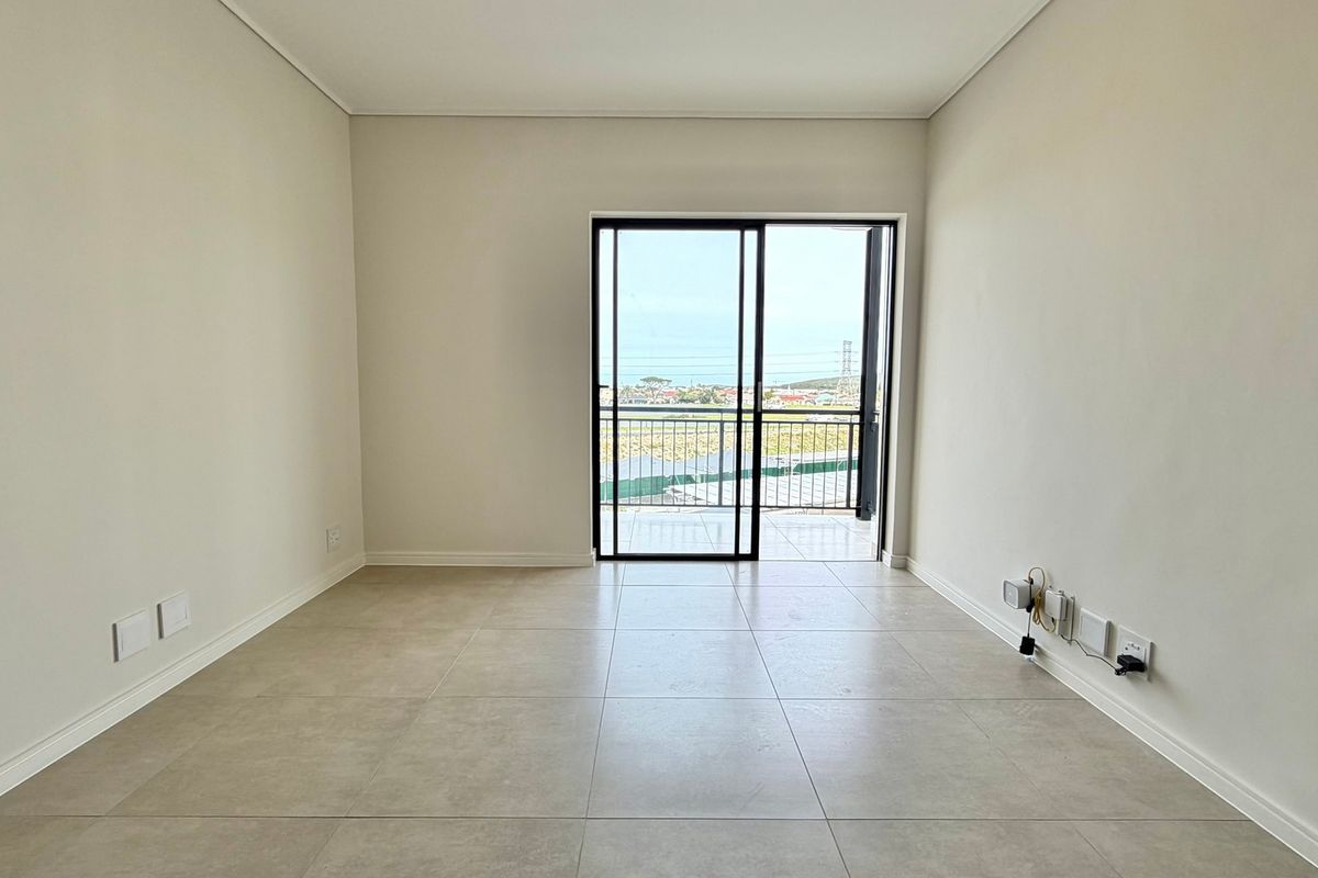 A bright, empty living area featuring neutral tiled flooring and a sliding glass door providing access to a balcony with scenic views.