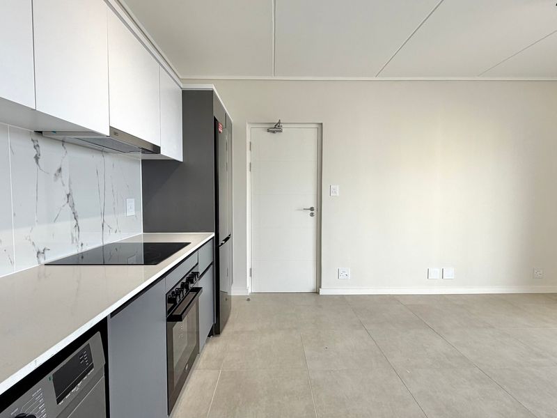 Modern open-plan kitchen featuring sleek cabinetry, stone countertops, marble-look splashback, and integrated appliances, flowing into a bright, tiled living area.