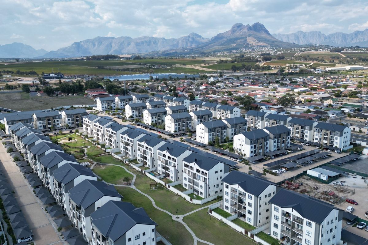 Aerial view of a modern residential apartment complex featuring multiple blocks, landscaped communal gardens, and covered parking facilities with mountain views.