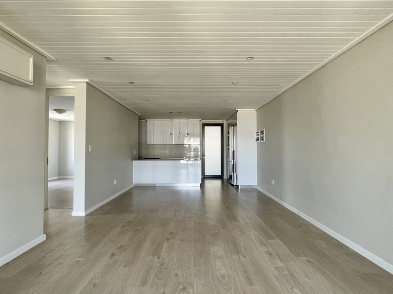 Spacious open-plan living area featuring light laminate flooring, recessed lighting, a wall-mounted air conditioning unit, and a modern kitchen with white cabinetry.